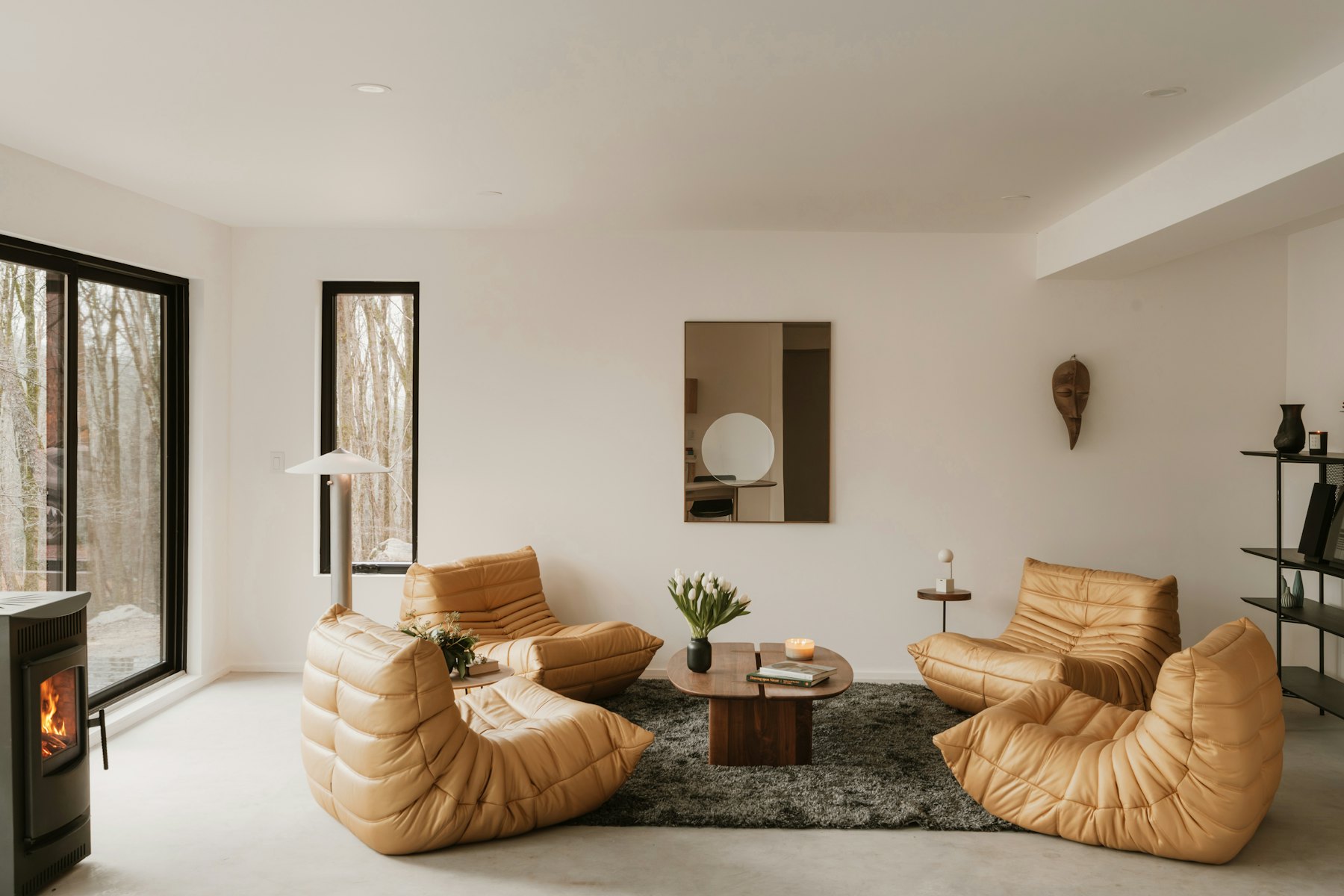 A bright living room with tan lounge chairs around a low table and a black wood stove