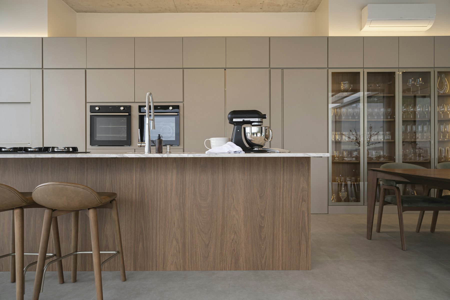 A walnut island with stools in front of a wall of warm grey cabinets