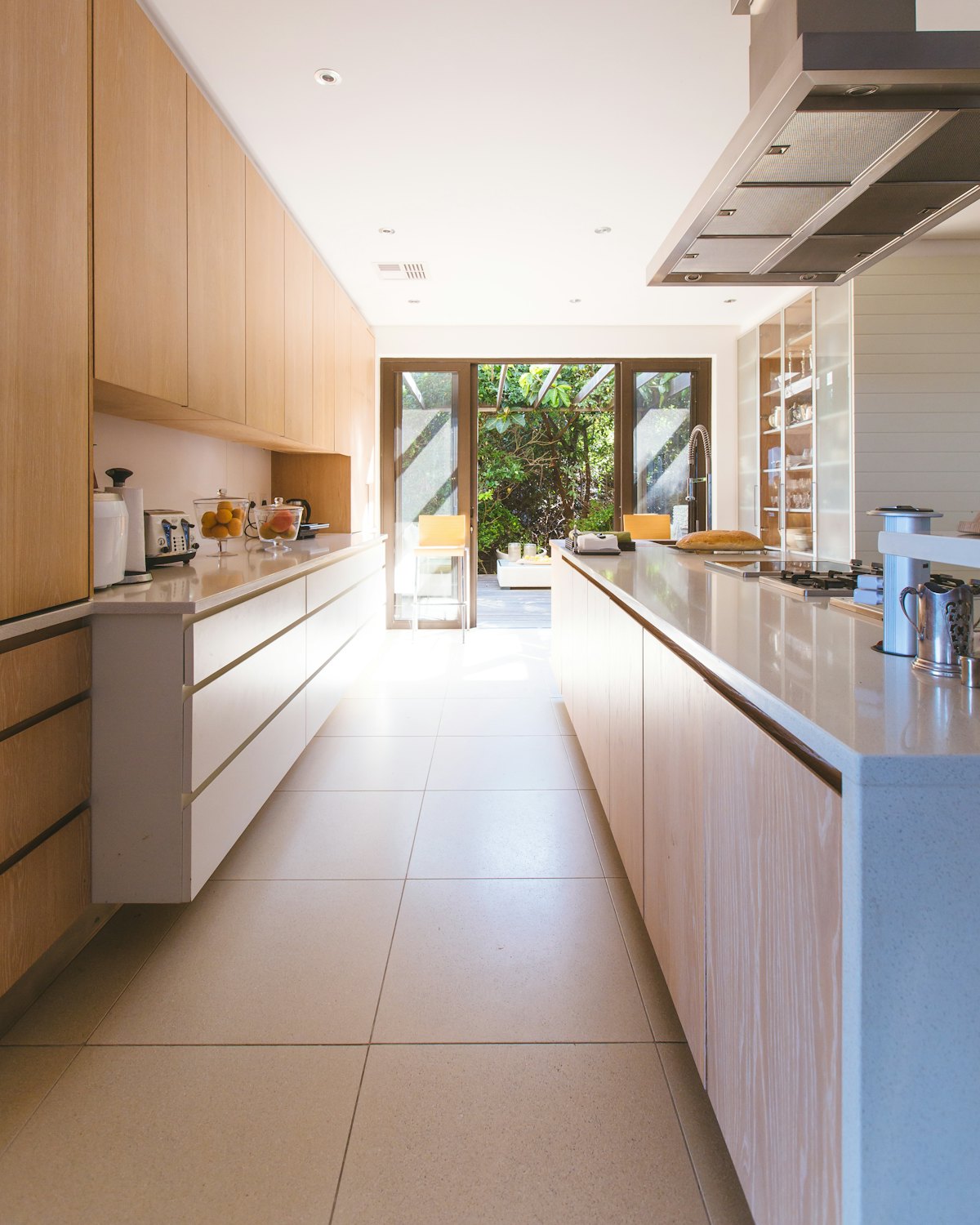 A narrow galley kitchen in pale oak leading to a sunny window