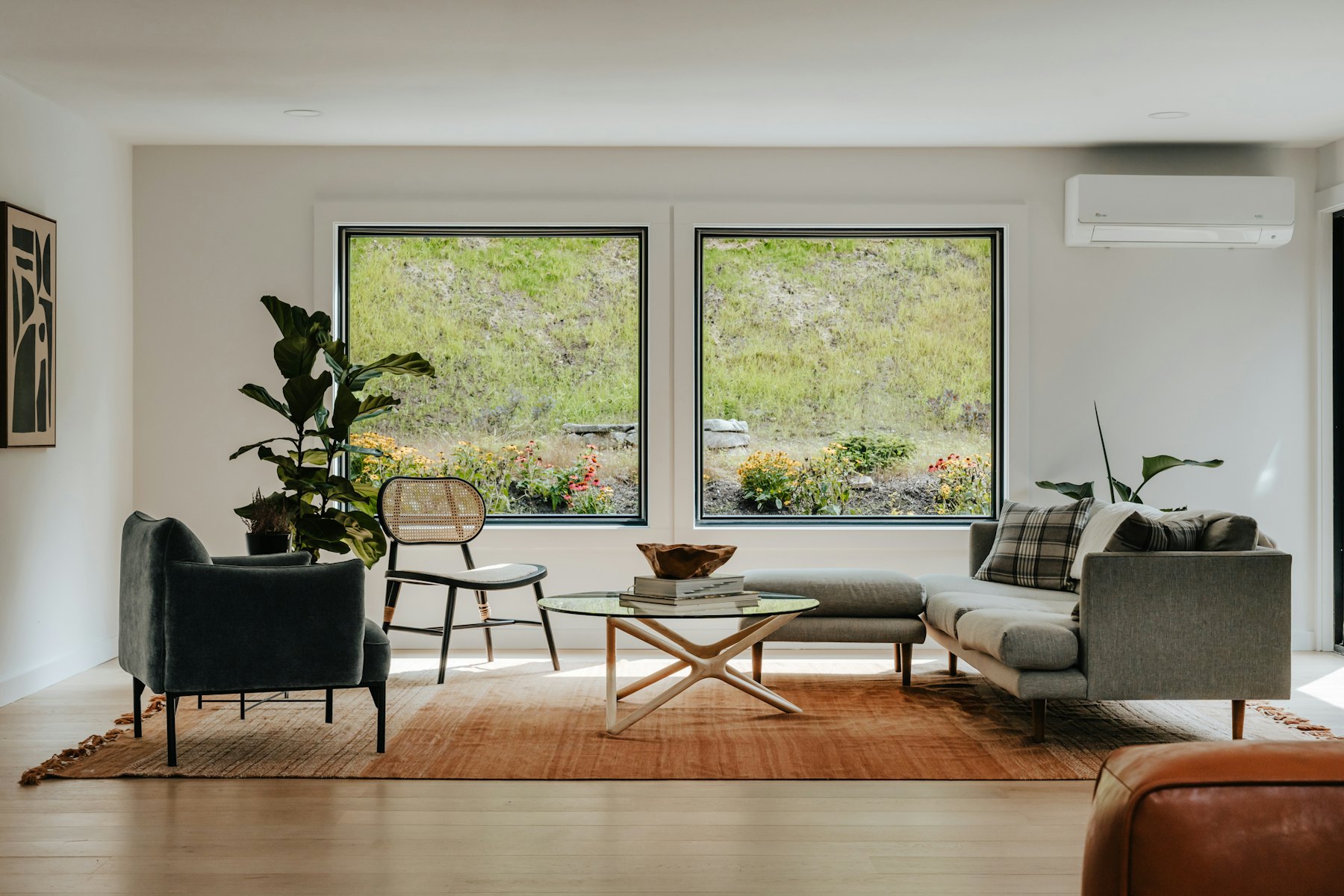 A living room with a grey sofa, a wooden coffee table and two large windows onto green trees