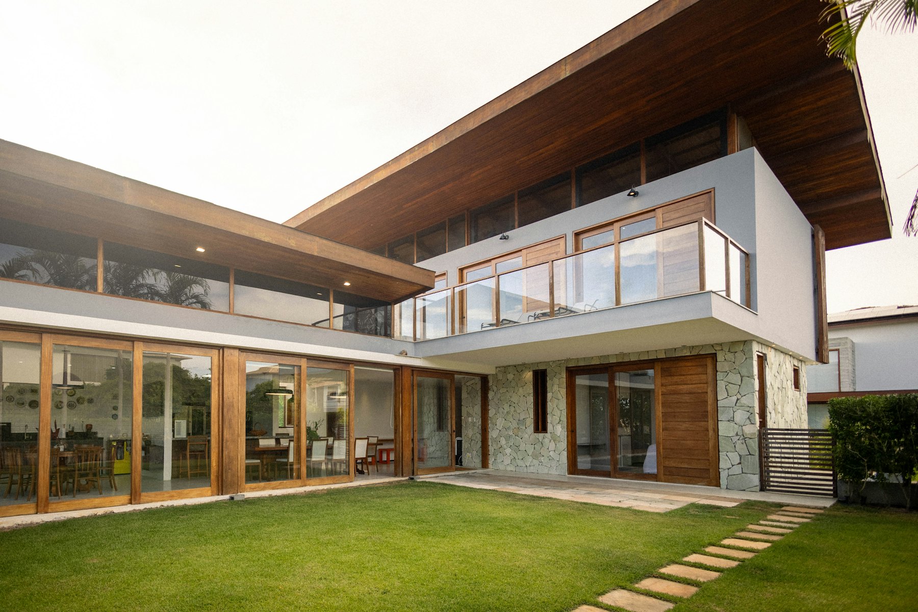A modern two storey house with a deep timber roof, stone walls and a green lawn