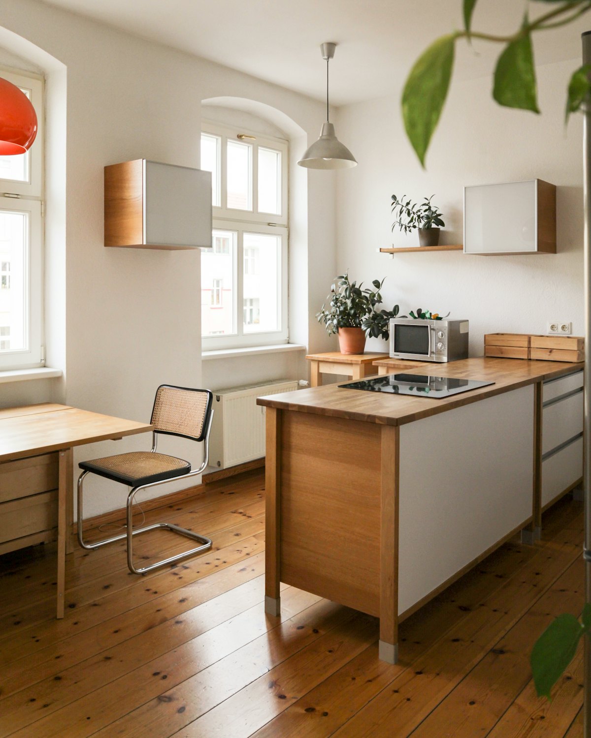 A small kitchen with a wooden table and tall white windows