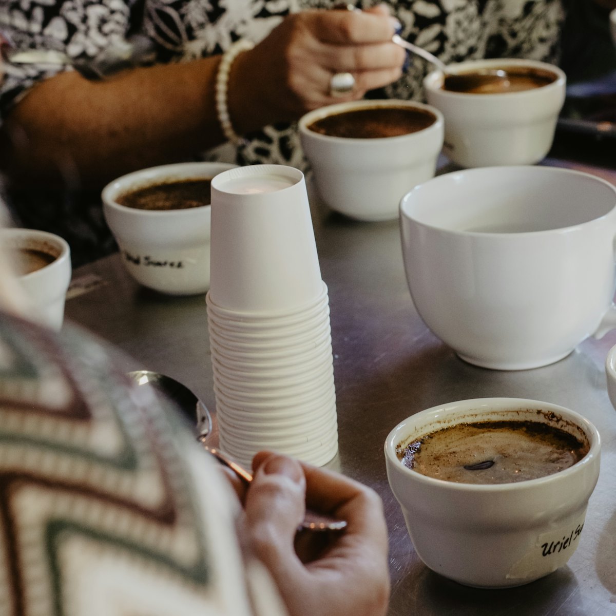 Rows of coffee cups and spoons laid out on a table for a cupping