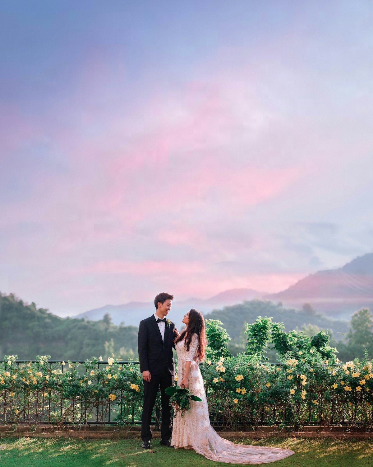 The couple standing at the edge of a vineyard under a pink evening sky
