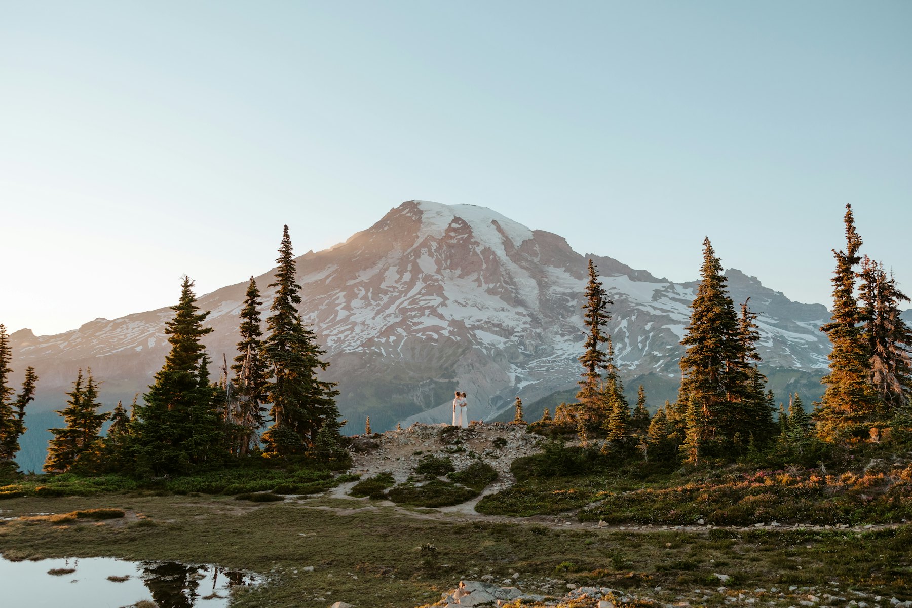 The couple small beneath a snowy peak and a stand of pines