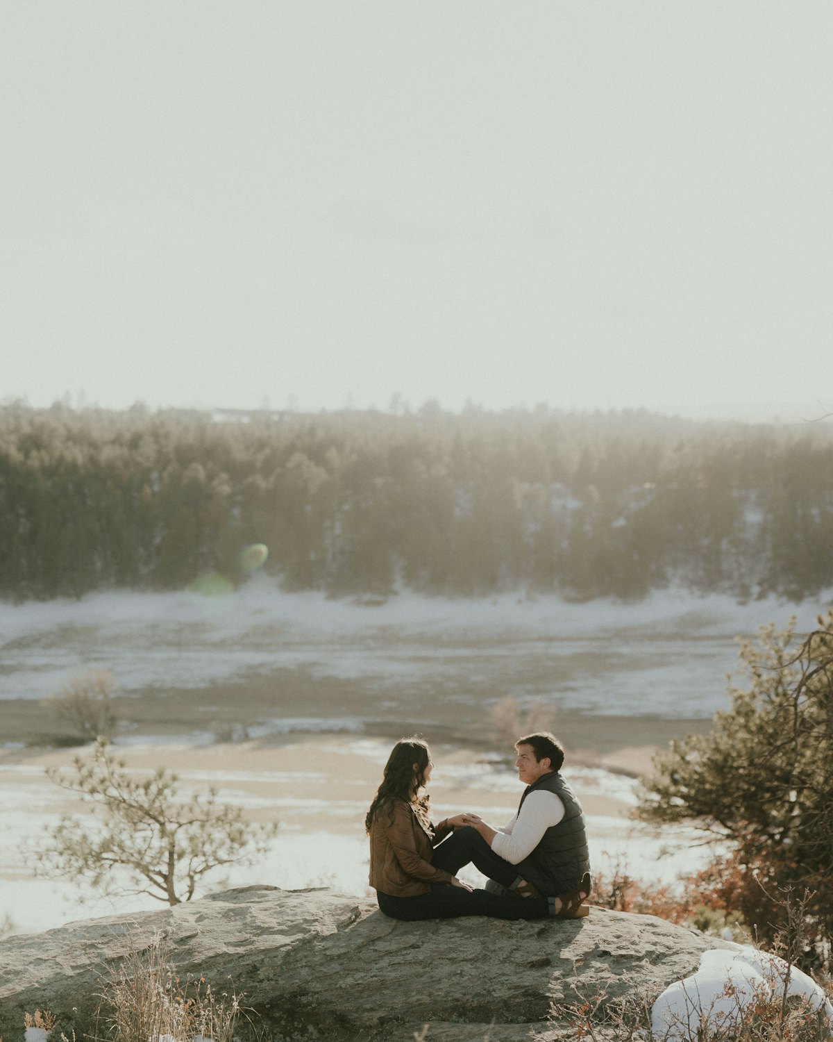 The couple sitting together on a rock by the frozen lake