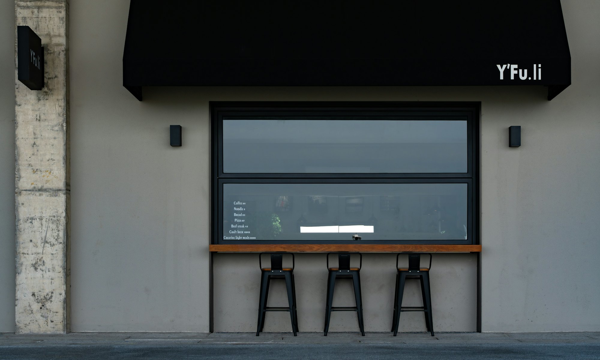 The front of the restaurant with stools under a black awning